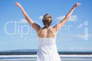Pretty blonde standing with arms outstretched on the beach