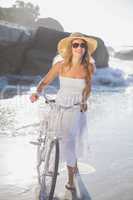Beautiful smiling blonde in sundress with her bike at the beach