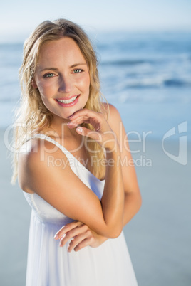 Pretty blonde standing at the beach in white sundress smiling at