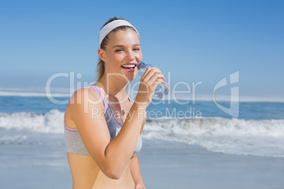 Sporty happy blonde drinking water on the beach