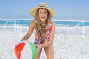 Fit laughing blonde in white bikini and straw hat holding beach