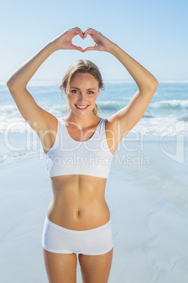 Gorgeous fit blonde making heart shape with hands by the sea