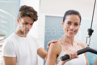 Fit smiling woman using weights machine for arms with her traine