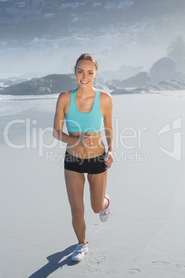 Fit woman smiling and jogging on the beach