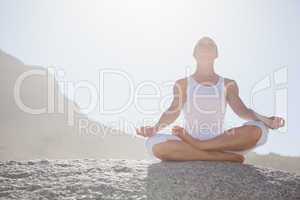 Blonde woman sitting in lotus pose on beach