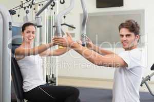 Fit brunette using weights machine for arms with trainer helping