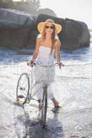 Beautiful smiling blonde in sundress on bike at the beach