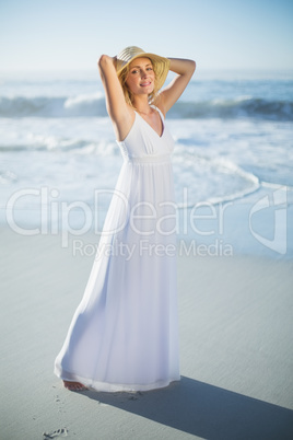 Smiling blonde standing at the beach in white sundress and sunha