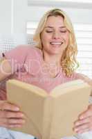 Happy blonde relaxing on the couch with book