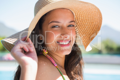 Beautiful brunette sitting by pool wearing straw sunhat