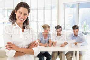 Casual businesswoman smiling at camera with team behind her