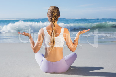 Sporty blonde sitting in lotus pose on the beach