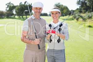 Golfing couple smiling at camera holding clubs