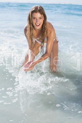 Beautiful smiling woman in white bikini splashing on the beach