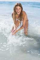 Beautiful smiling woman in white bikini splashing on the beach