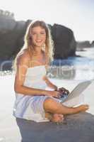 Beautiful smiling blonde in sundress using tablet on the beach