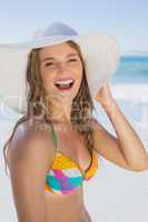 Beautiful girl in bikini and straw hat smiling at camera on beac