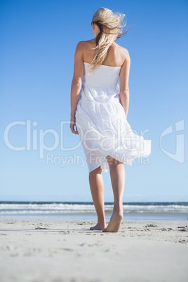 Blonde in white dress strolling on the beach