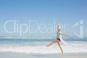 Fit woman jumping gracefully on the beach with scarf