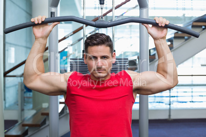 Handsome bodybuilder using weight machine for arms