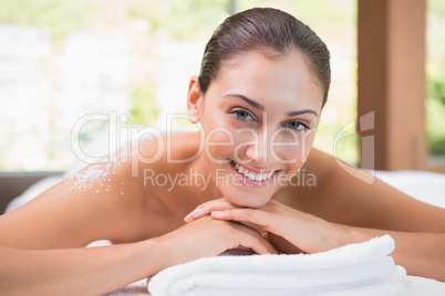 Beautiful smiling brunette lying on massage table with salt scru Beautiful smiling brunette lying on massage table with salt scru