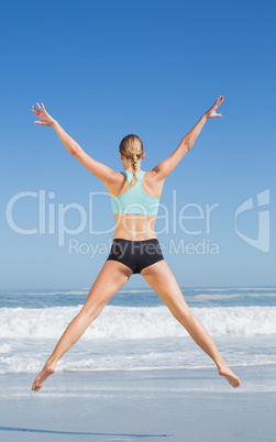 Fit woman jumping on the beach with arms out