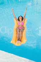 Excited woman in pink bikini lying on lilo in swimming pool