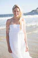 Woman in white dress smiling at camera on the beach