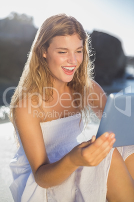 Beautiful smiling blonde in sundress using tablet on the beach