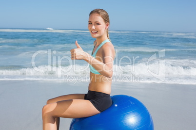 Fit woman sitting on exercise ball at the beach smiling at camer