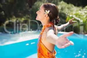 Brunette in sarong smiling by the pool with arms outstretched