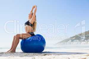 Fit blonde sitting on exercise ball at the beach