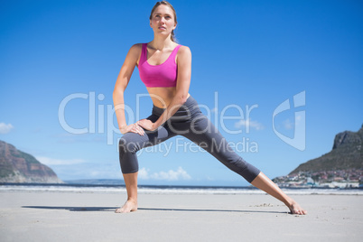 Focused fit blonde warming up on the beach