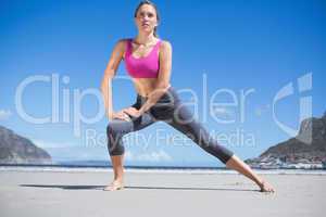 Focused fit blonde warming up on the beach