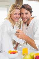 Cute couple in bathrobes having breakfast together smiling at ca