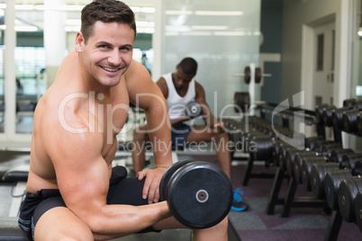 Handsome bodybuilder lifting heavy dumbbell smiling at camera