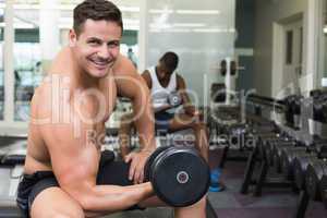 Handsome bodybuilder lifting heavy dumbbell smiling at camera