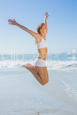 Gorgeous fit blonde jumping by the sea with arms out