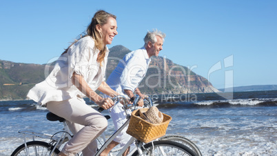 Smiling couple riding their bikes on the beach