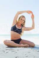 Fit blonde in yoga pose on the beach smiling at camera