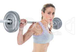 Strong female crossfitter lifting barbell behind head looking at