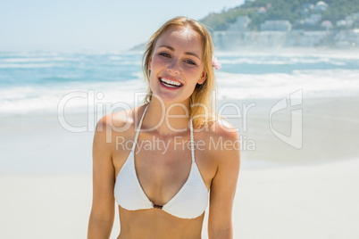 Beautiful blonde in white bikini smiling at camera on the beach