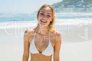 Beautiful blonde in white bikini smiling at camera on the beach