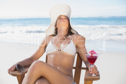 Pretty blonde relaxing in deck chair on the beach with cocktail