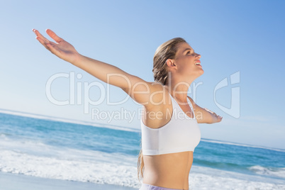 Sporty blonde standing on the beach with arms out