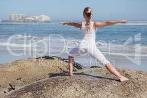 Blonde woman standing in warrior pose on beach on rock