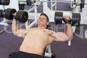 Shirtless bodybuilder lifting heavy dumbbells lying on bench