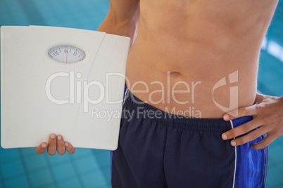 Fit man in swimming trunks standing by the pool holding weighing