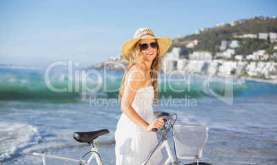 Beautiful smiling blonde in sundress with her bike at the beach