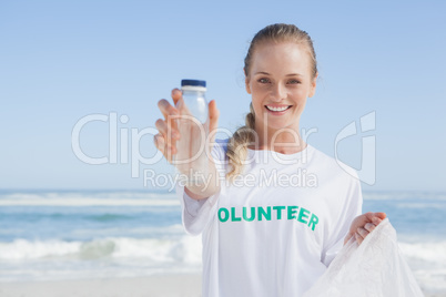 Blonde smiling volunteer picking up trash on the beach